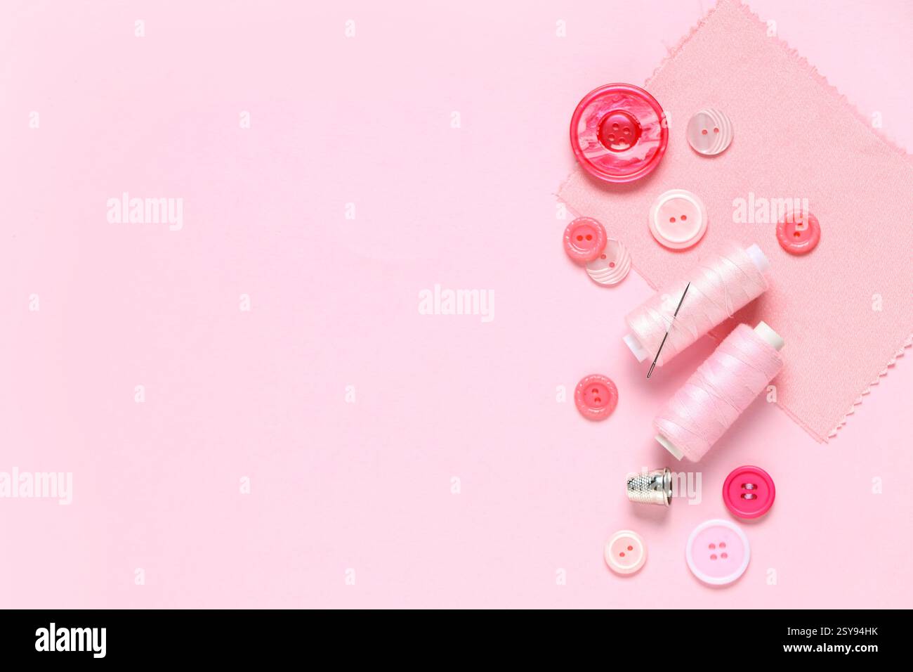 Different colorful buttons with thread spools and fabric sample on pink background Stock Photo