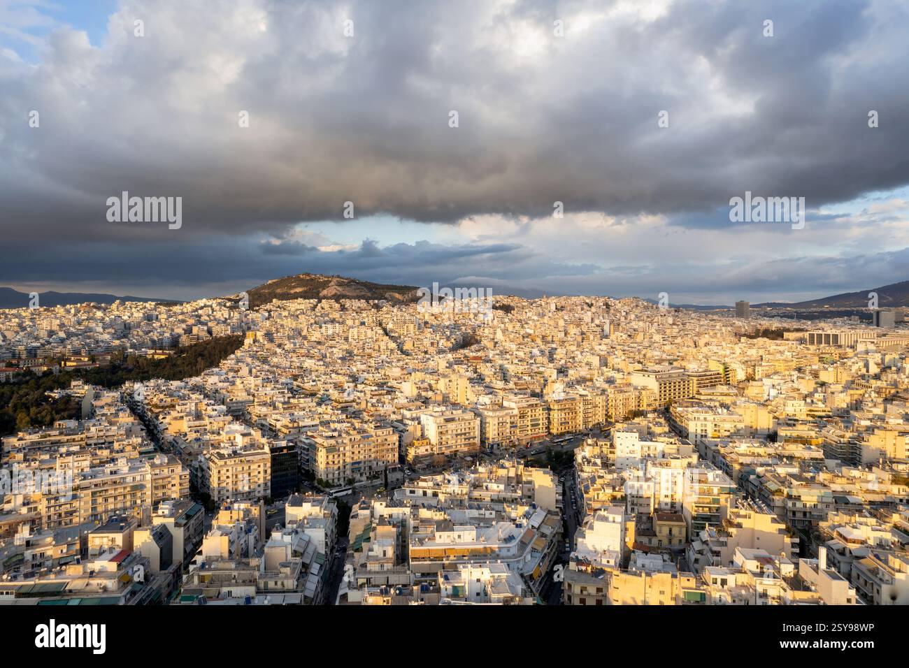 Athens aerial view over Eksarhia, Neapoli and Alexandras Avenue below big, dark clouds during golden hour. Stock Photo