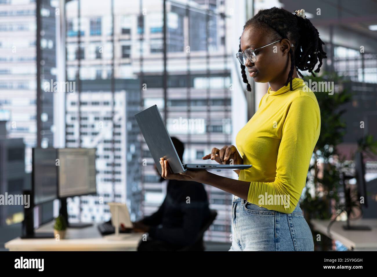 Cybersecurity expert using laptop to look for company security vulnerabilities, comparing with computer monitors. Programmer installing fortified code on laptop, crosschecking with PC screens Stock Photo