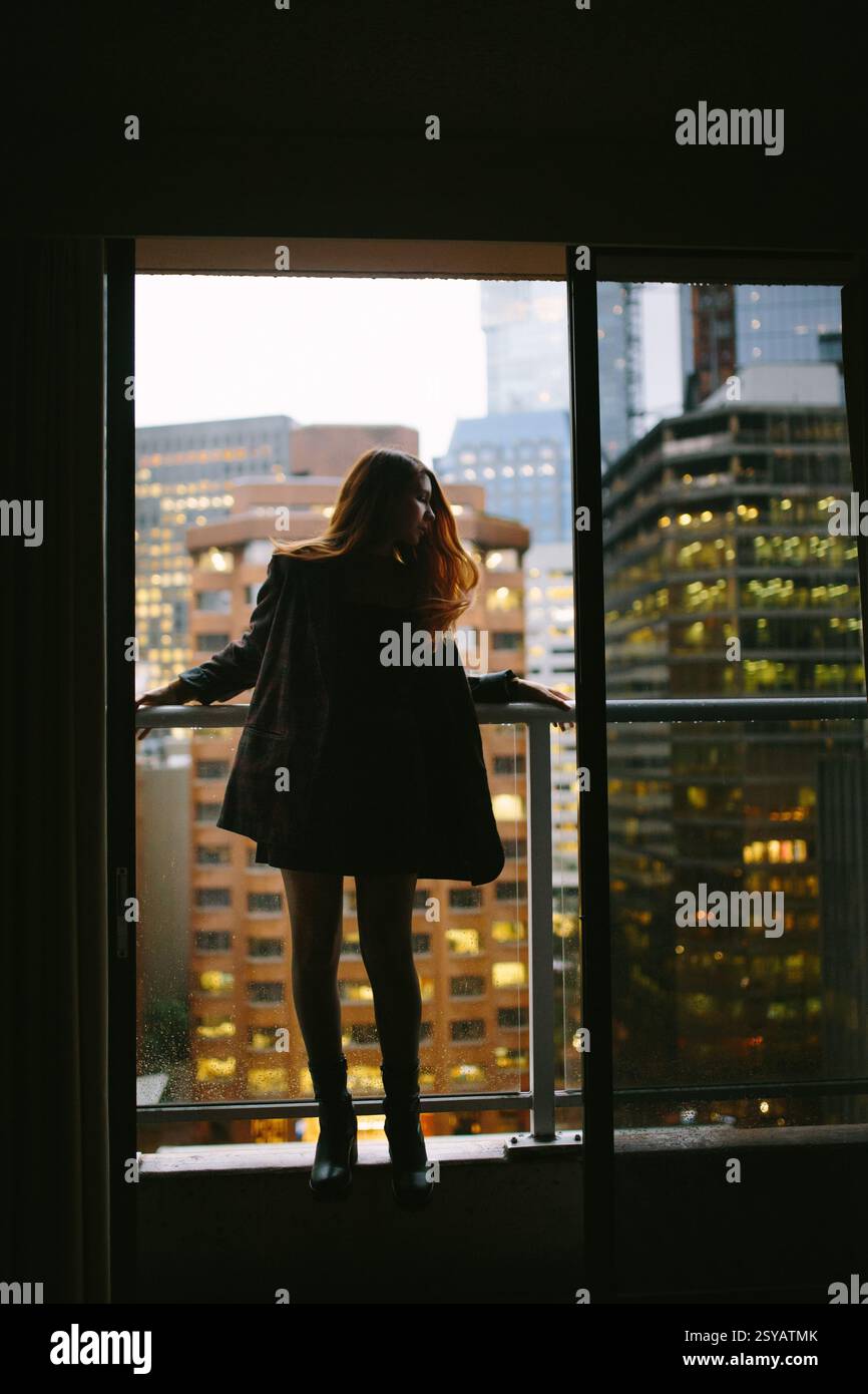 A redhead woman standing by a window, overlooking a bustling cityscape ...