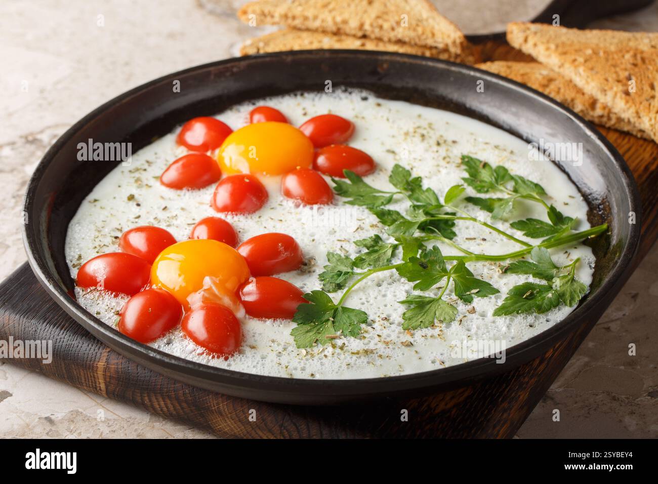 Flower shaped breakfast idea cooked fried eggs, parsley and cherry tomatoes close-up in a plate on the table. Horizontal Stock Photo