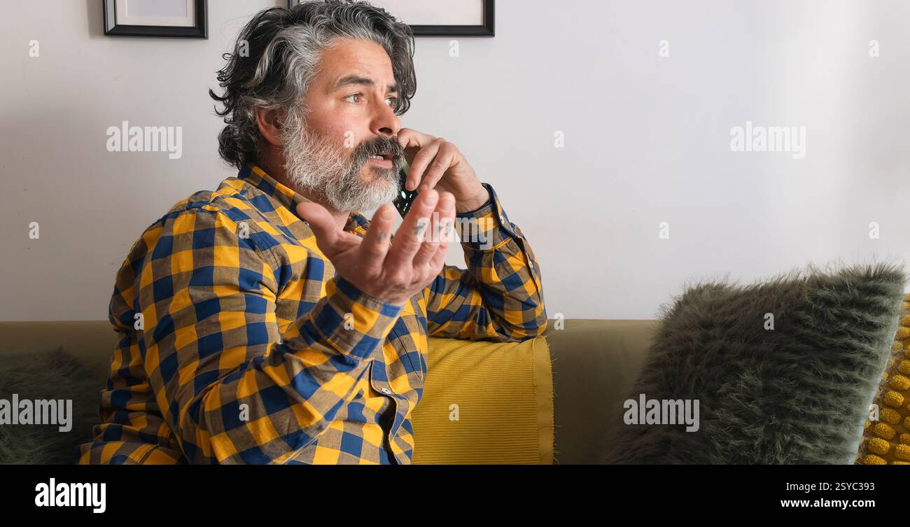 Bearded man gesturing while talking on smartphone at home Stock Photo