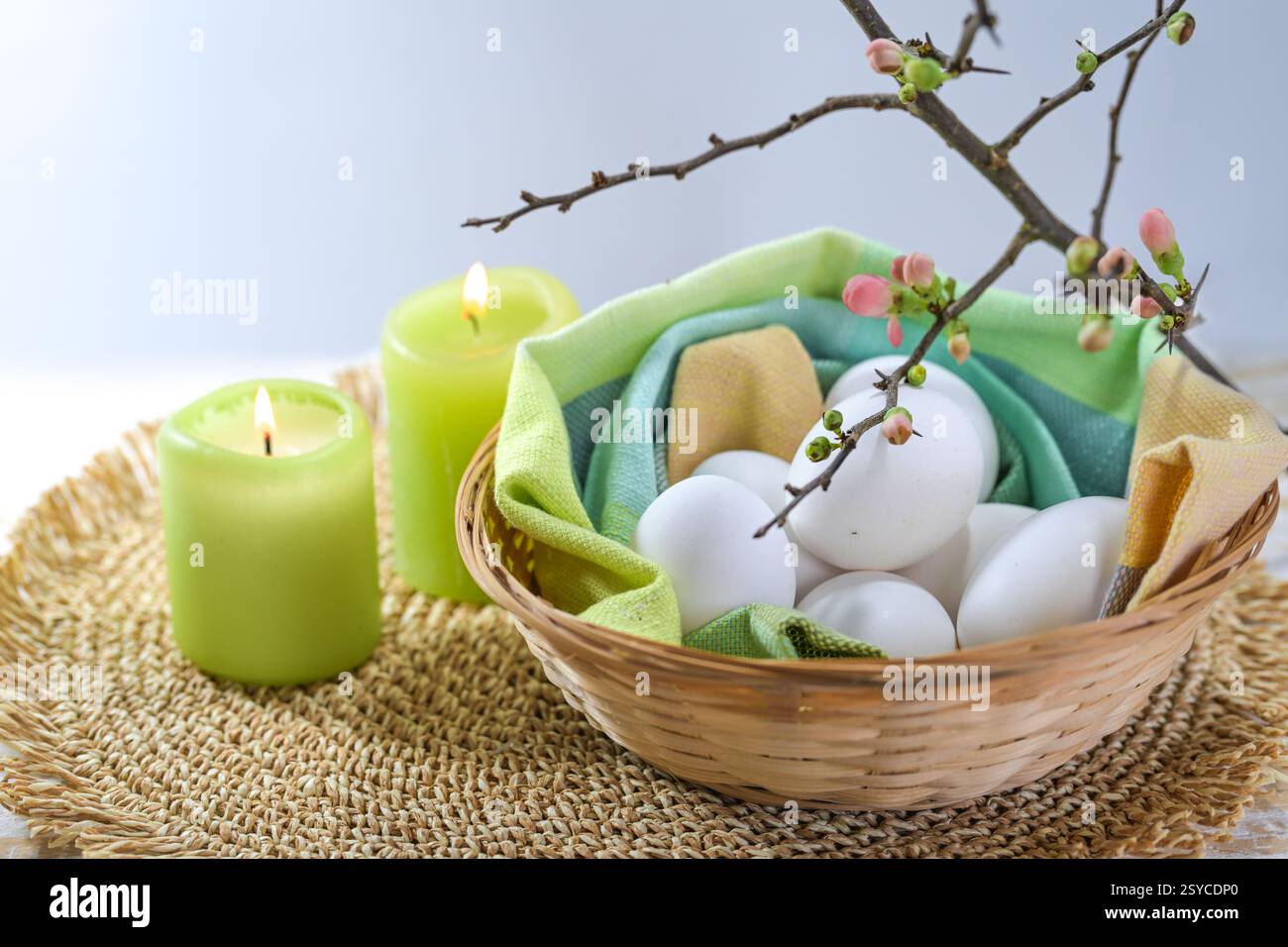 White eggs for Easter holidays in a small basket with a napkin, green candles and a blooming quince branch, copy space, high angle view from above, se Stock Photo
