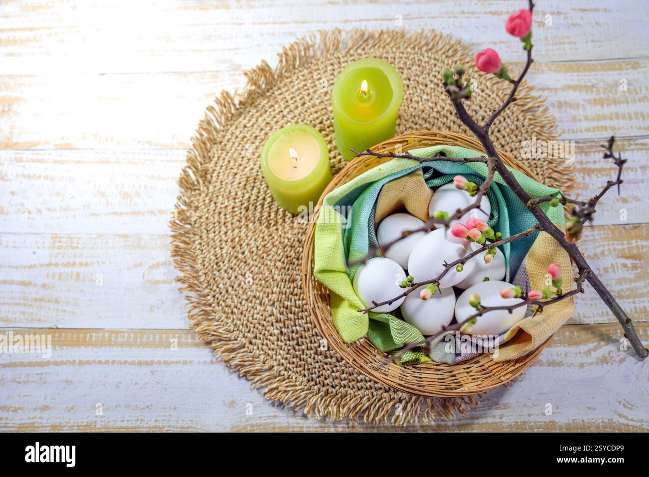 Easter arrangement with white eggs in a basket with a napkin, green candles and a blooming quince branch, copy space, high angle view from above, sele Stock Photo