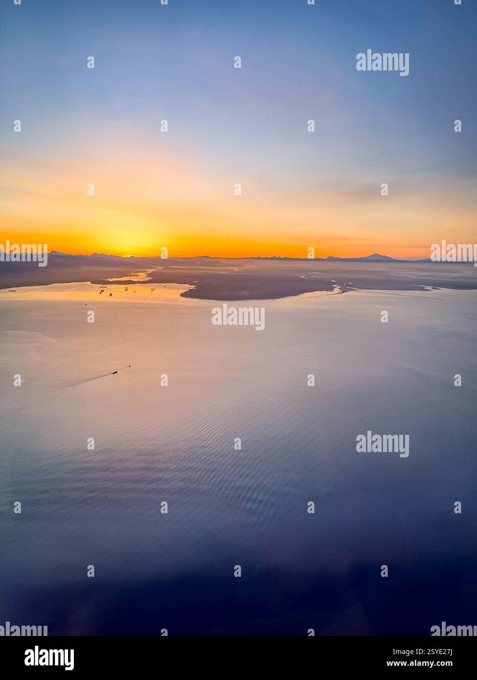 Aerial view of the ocean with small islands at sunrise. The golden glow reflects off the water, blending warm and cool tones across the vast coastal h Stock Photo
