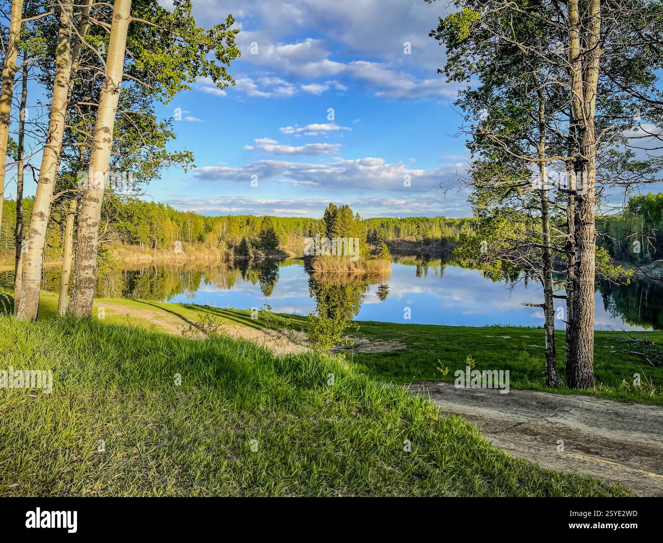 A peaceful lake reflecting surrounding trees and a partly cloudy sky during sunset. The lush greenery along the shoreline adds to the scenic outdoor b - Smartphone Captured Stock Image