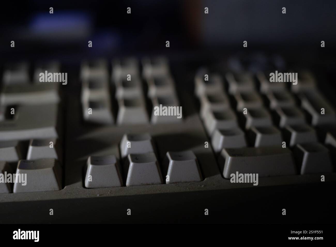 This close-up view captures a vintage computer keyboard covered in dust against a dimly lit background. The worn keys suggest years of usage during la Stock Photo