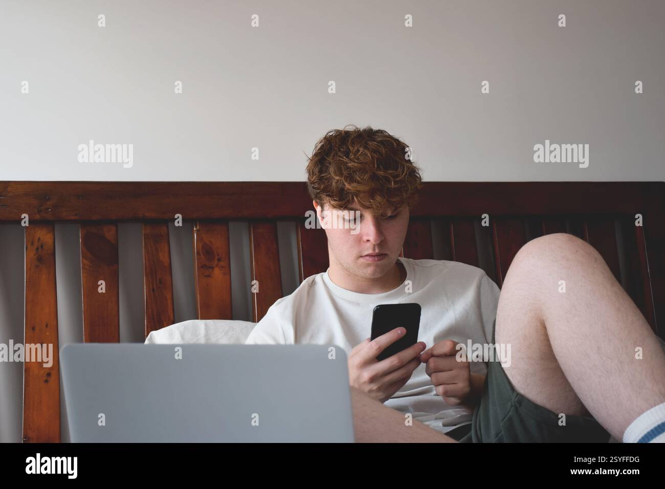 Young man sitting on bed using mobile phone Stock Photo