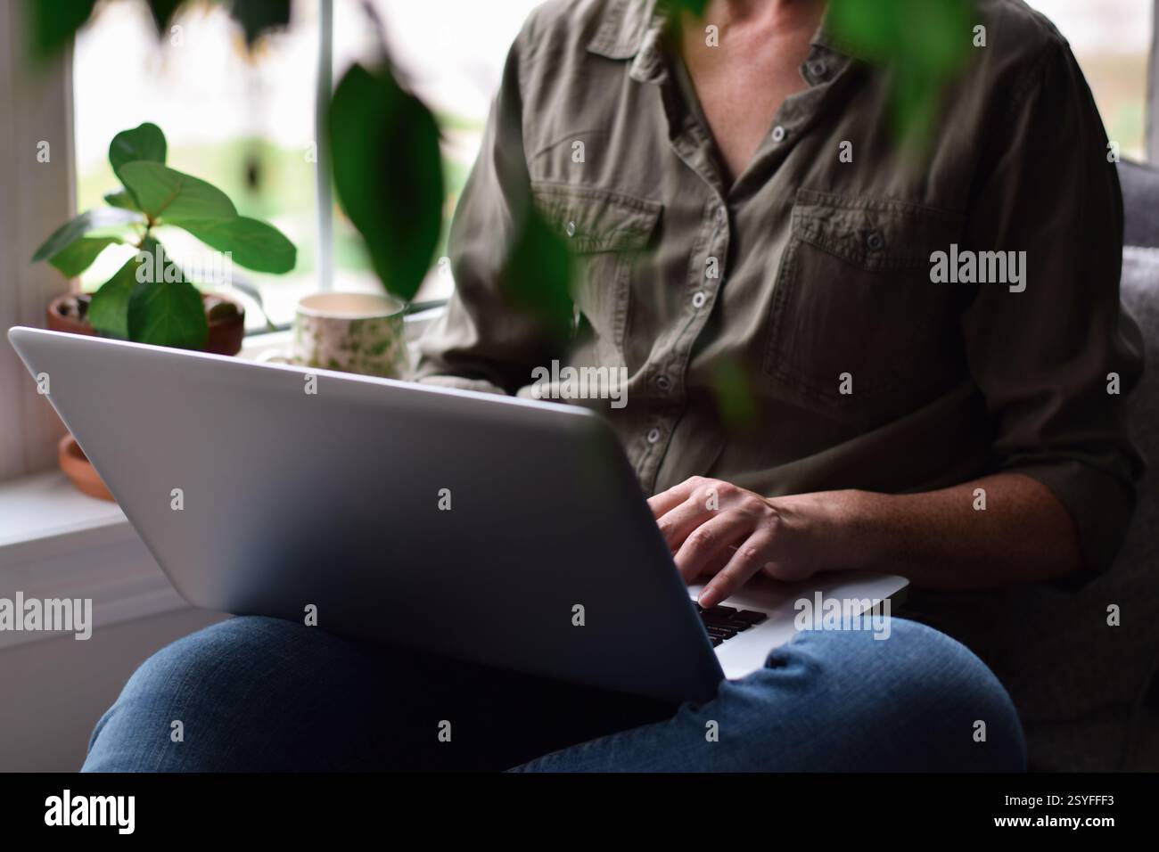 Woman sitting by a window at home using laptop computer Stock Photo