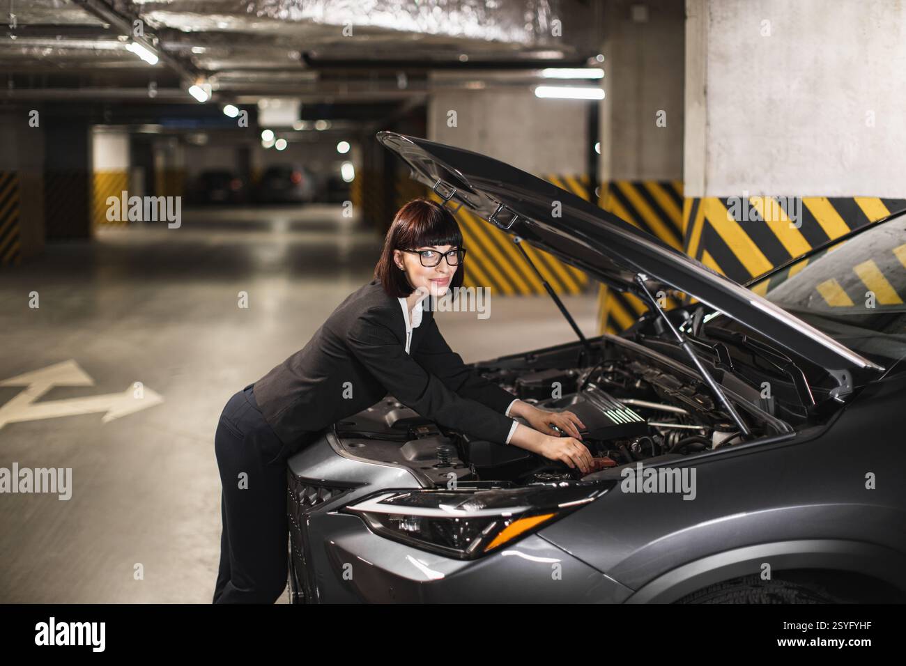 Caucasian businesswoman in formal attire fixes car engine in dimly lit ...