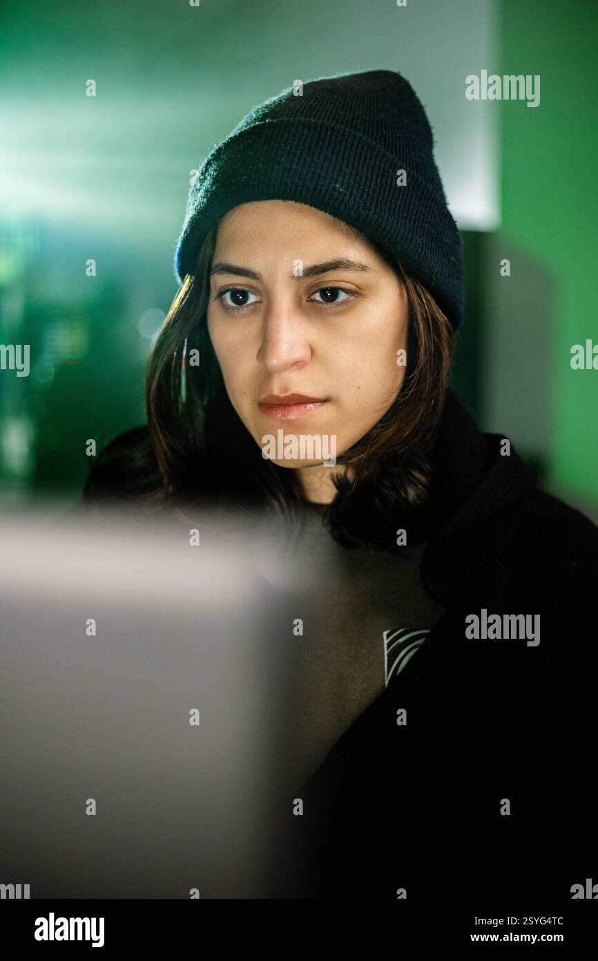 Female young hacker working on computer in dark room programming code Stock Photo