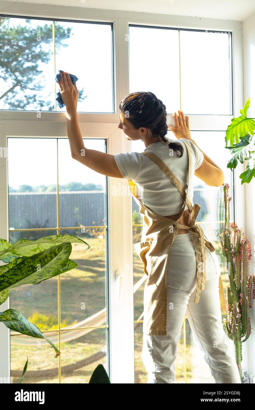 Woman in apron manually washes the window of house with rag cleaner and ...