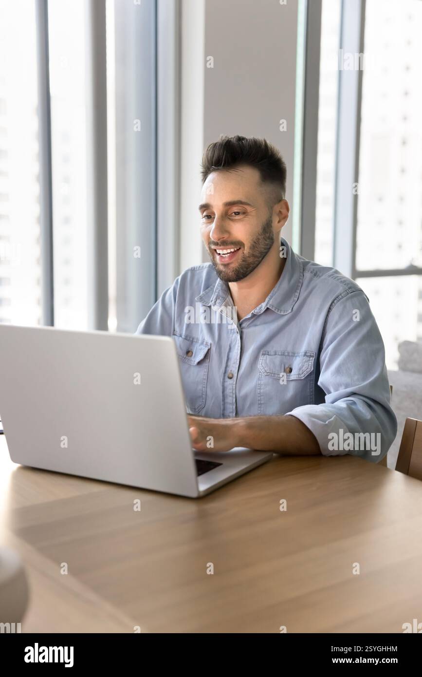 Smiling man sitting at desk working on studying using laptop Stock Photo
