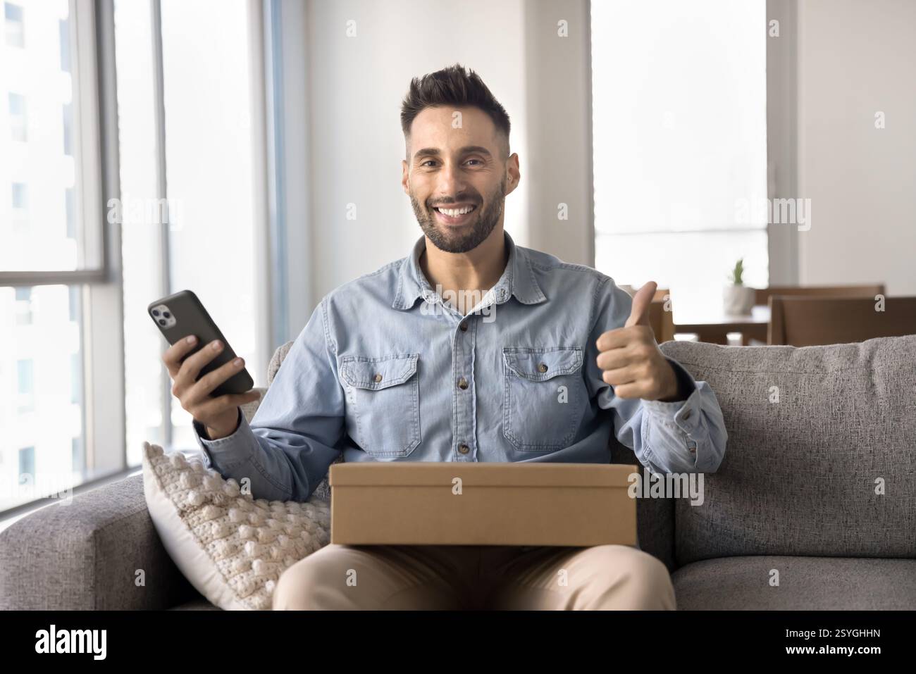 Man holds phone and box smiling at camera, showing thumbs-up Stock Photo