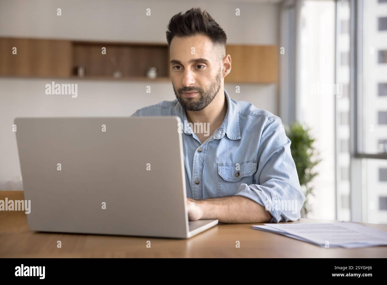 Handsome focused man sits at desk using laptop Stock Photo