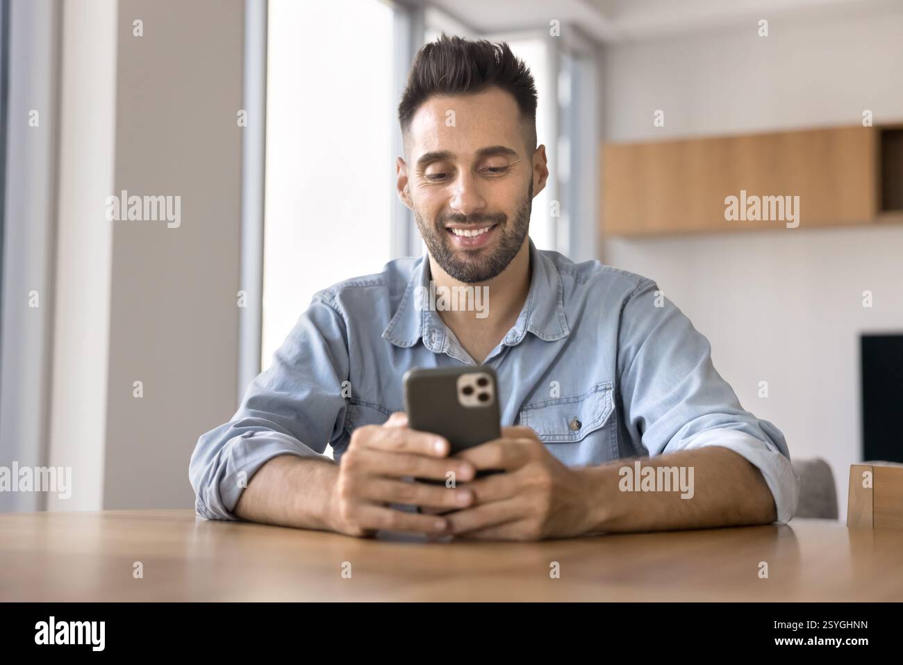 Hispanic man using his smartphone seated at table at home Stock Photo