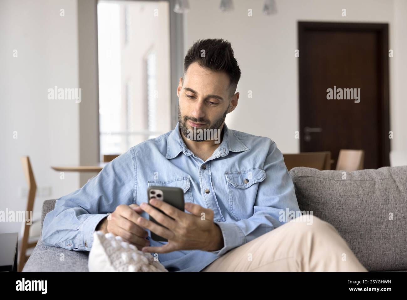 Hispanic man using his smartphone seated on sofa at home Stock Photo
