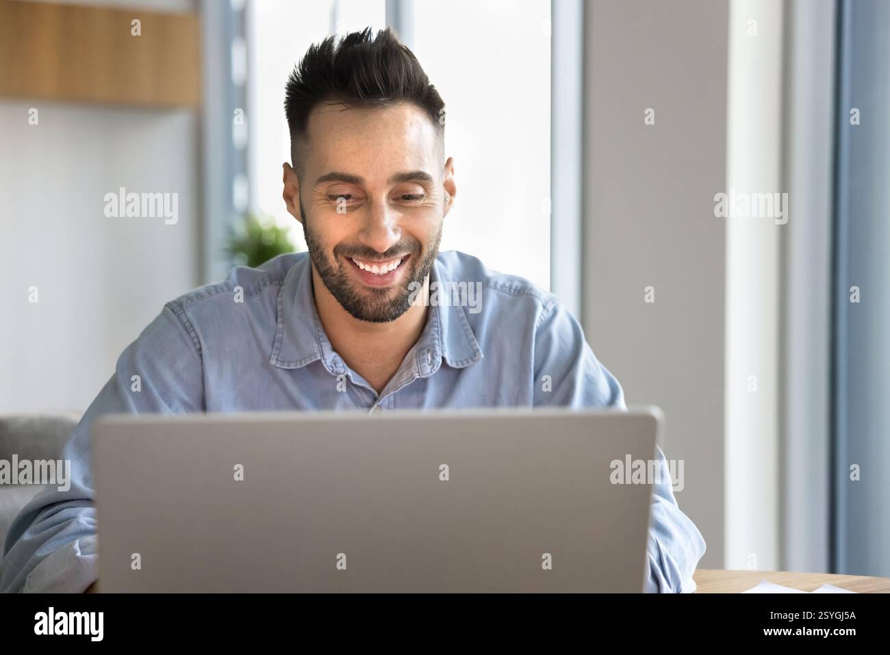 Smiling Latin man using laptop at home office Stock Photo