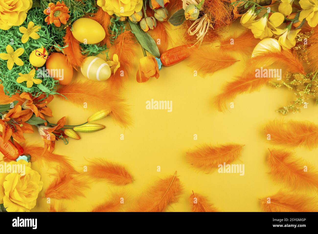 Orange feathers and flowers with Easter eggs on a yellow background Stock Photo