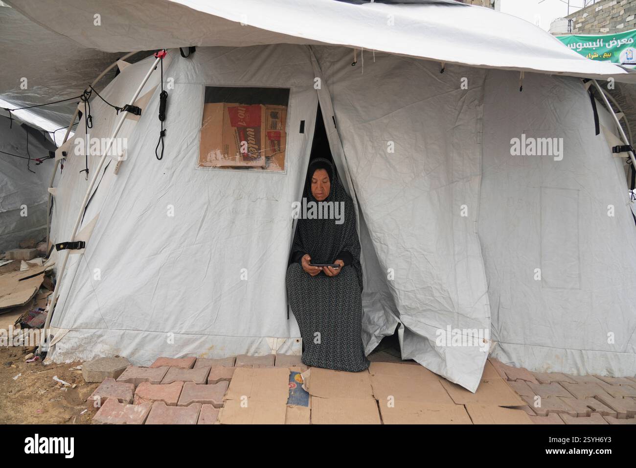 A displaced Palestinian woman sits in the doorway to her tent in a ...