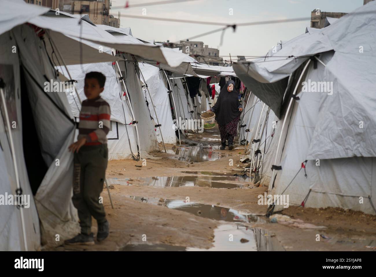A Palestinian woman carried a muddy bucket as she walks between tents ...
