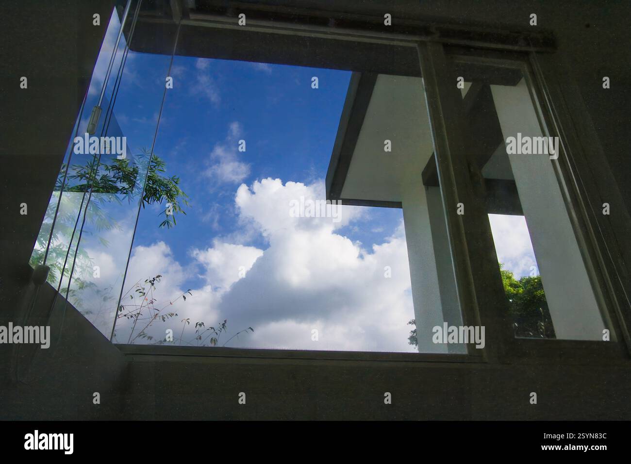 A window frames a bright blue sky with fluffy white clouds. The view is ...