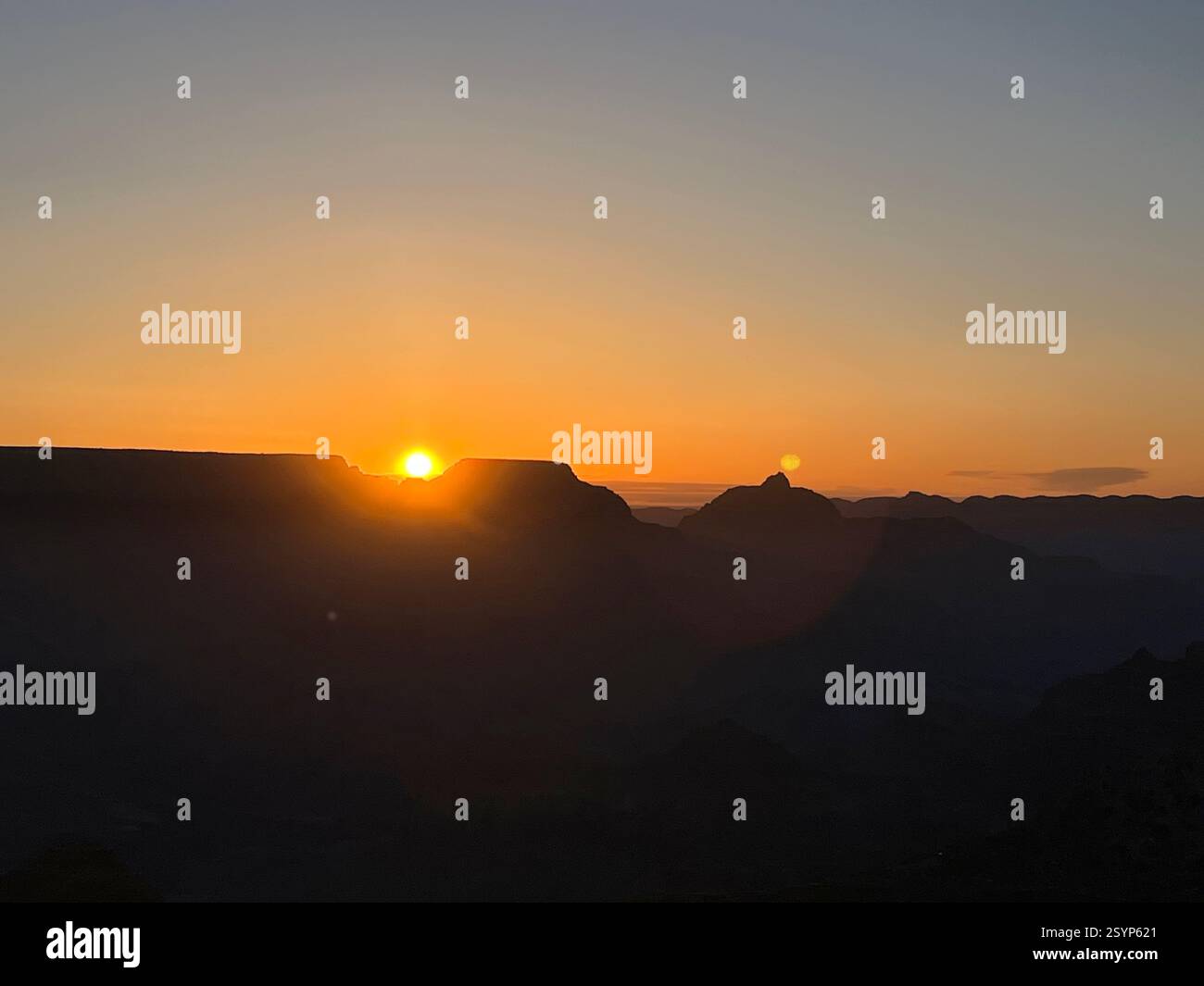 Golden sunlight touches the Grand Canyon’s horizon, leaving the rock formations in silhouette for a peaceful and majestic scene. - Smartphone Captured Stock Image