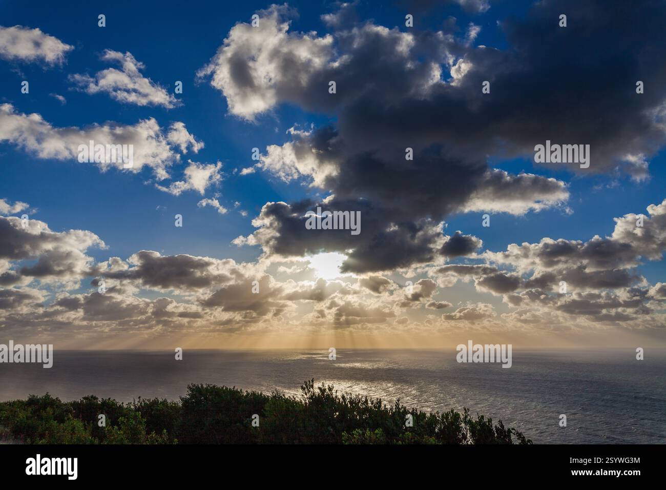 The sun breaks through dramatic clouds over a calm ocean, casting a ...