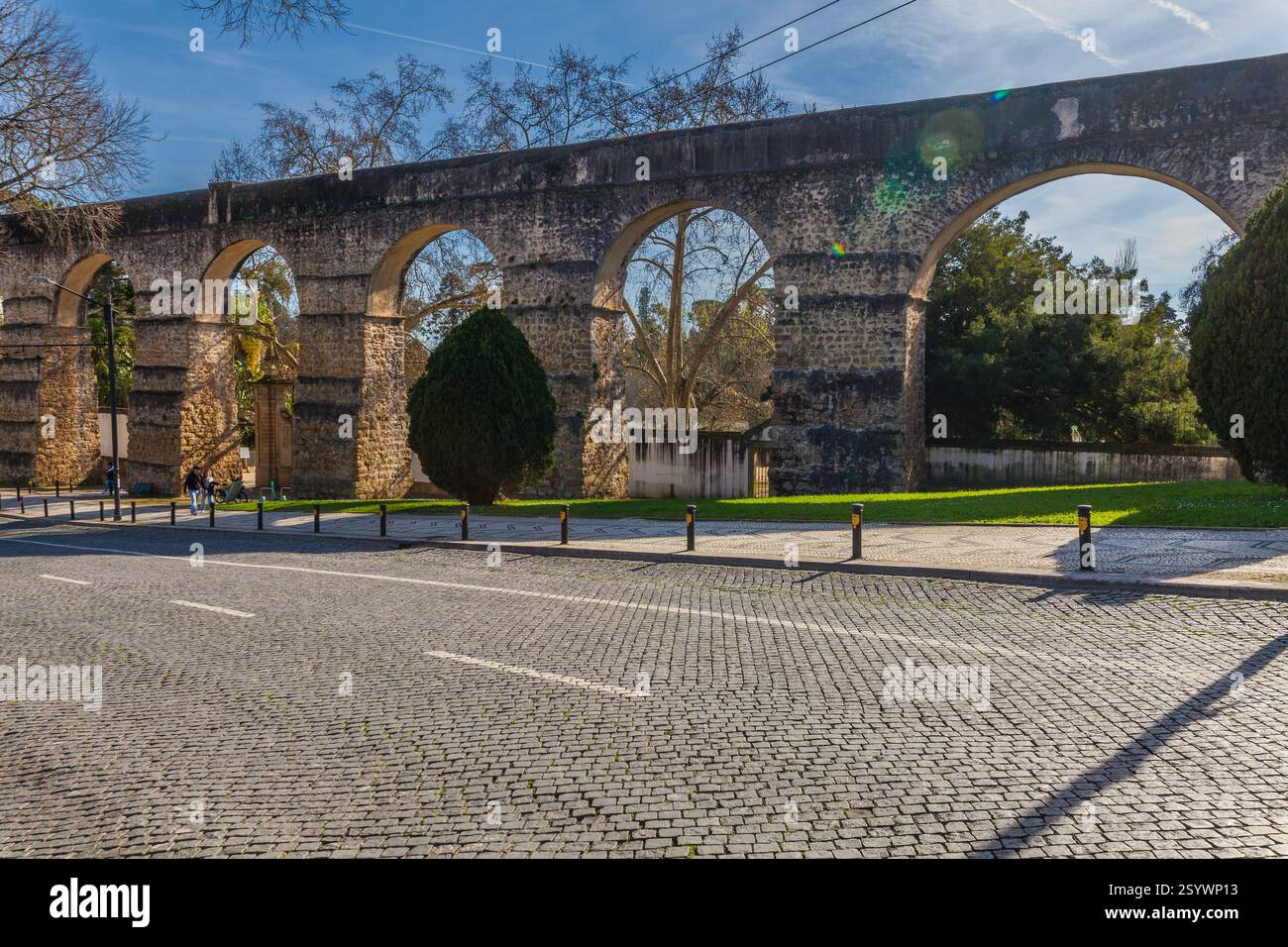 A historic stone aqueduct with arches spans across a modern street with ...