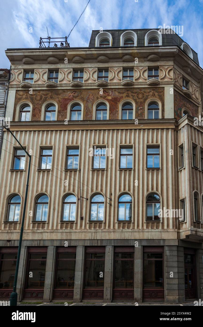 A multi-story building with a decorated facade featuring rows of arched windows, contrasting textures, and a dark-colored upper level under a cloudy s Stock Photo
