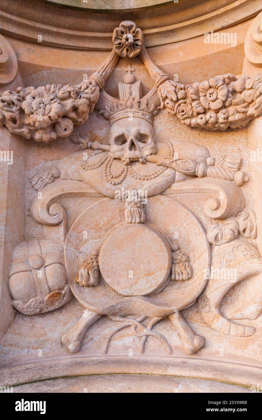 A close-up of an ornate stone carving featuring a skull, crossbones, a crown, and other decorative elements, set against a textured background., Charl Stock Photo