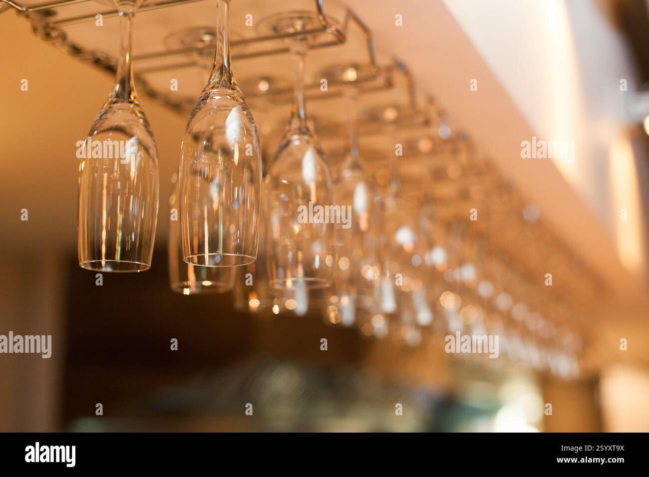 Empty wine glasses hang from a bar rack, likely in a restaurant or bar Stock Photo