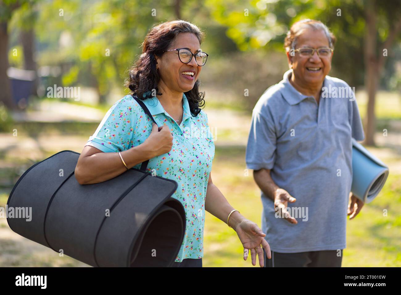Mature couple standing with yoga mat in public park Stock Photo