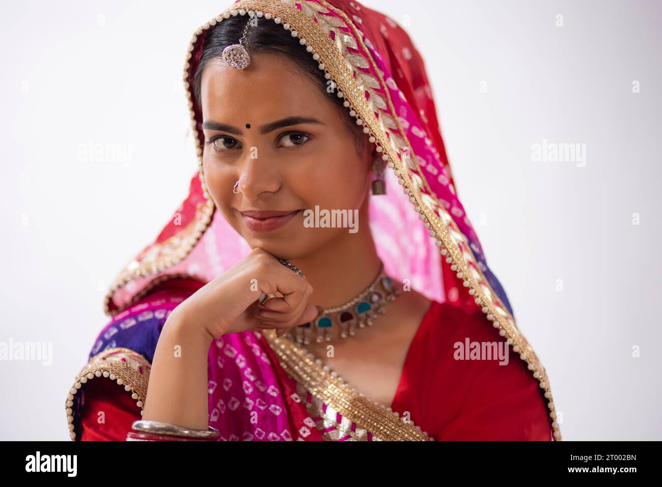 Close-up portrait of a cheerful Rajasthani young woman with hand on chin against white background Stock Photo