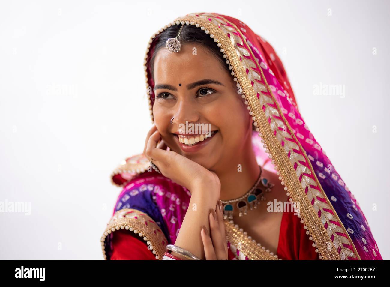 Close-up portrait of a smiling Rajasthani young woman with hand on cheek against white background Stock Photo