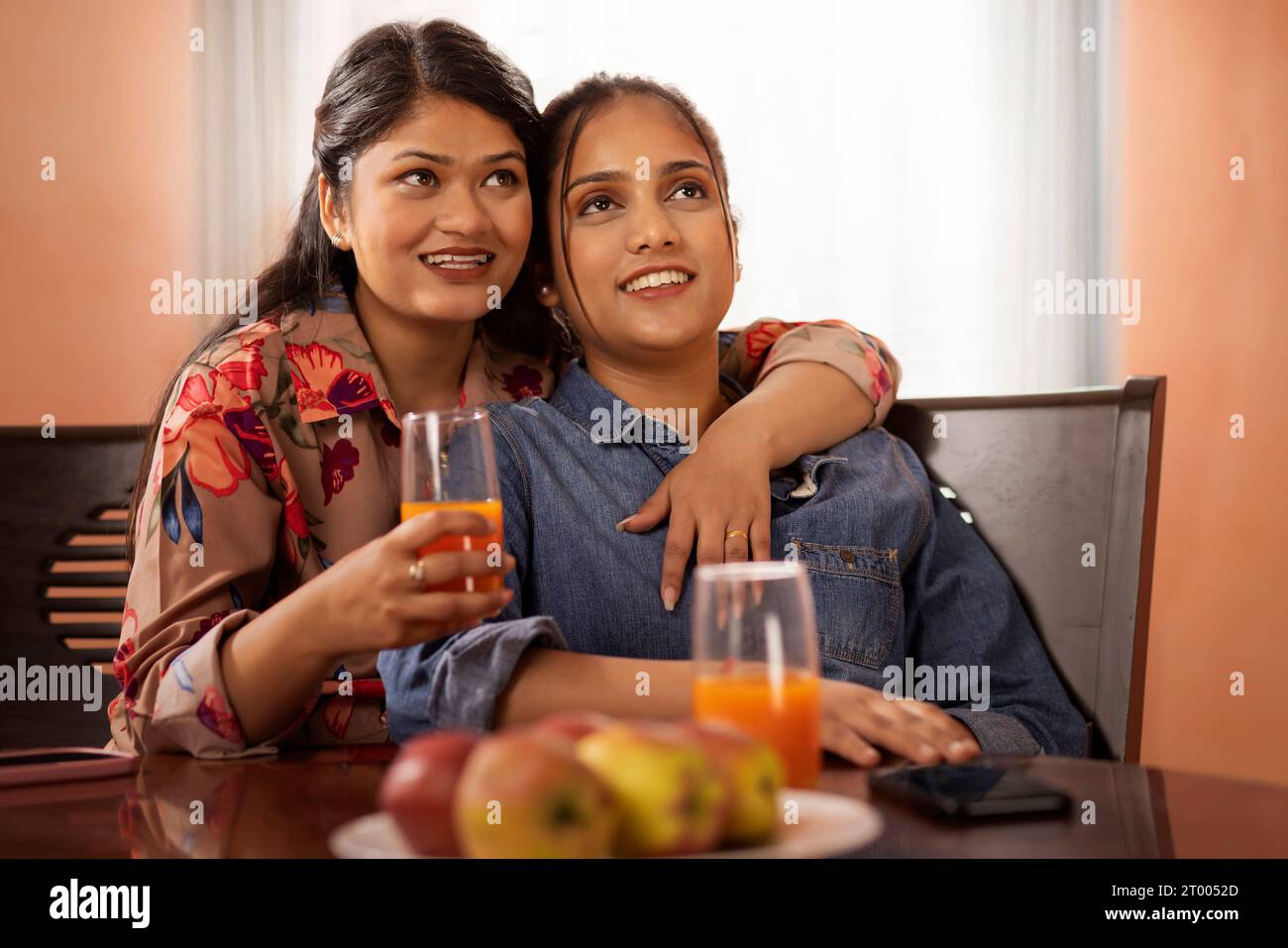 Two young women watching TV together as they sit on a dining table Stock Photo Alamy