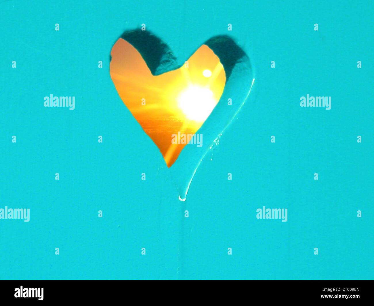 turquoise blue-green wooden wall with a cut sawn-out heart through which the sun shines like sundown, sunrise, sunset, for valentine, romatic wedding Stock Photo