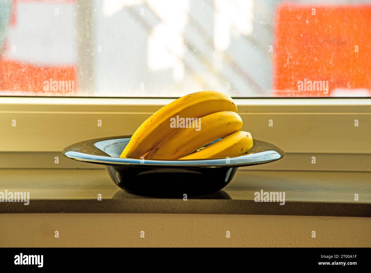 ripe bananas in a black fruit bowl on a window sills Stock Photo