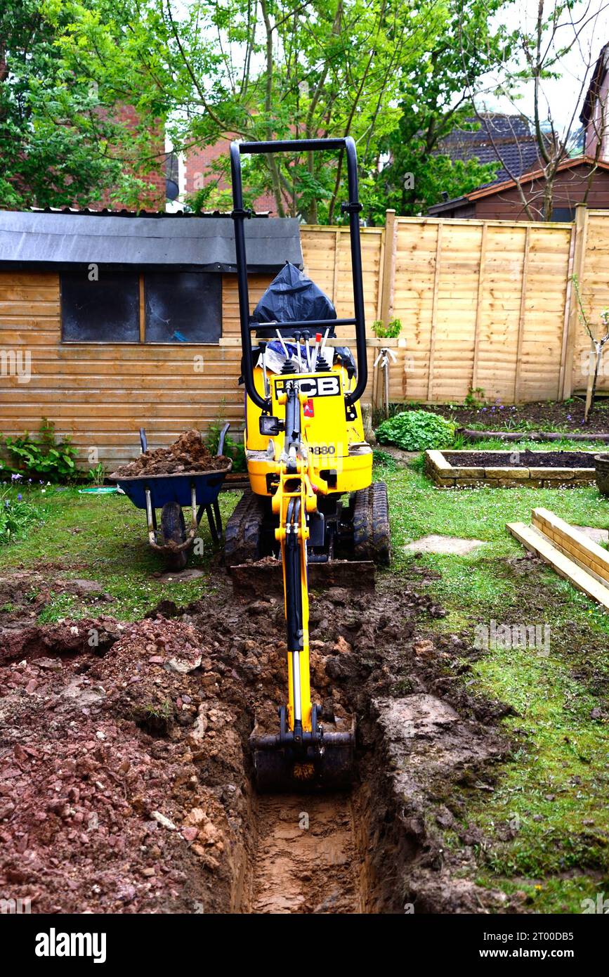 Mini digger parked in a garden being used for digging out ground to build a conservatory, Chard, Somerset, UK, Europe. Stock Photo