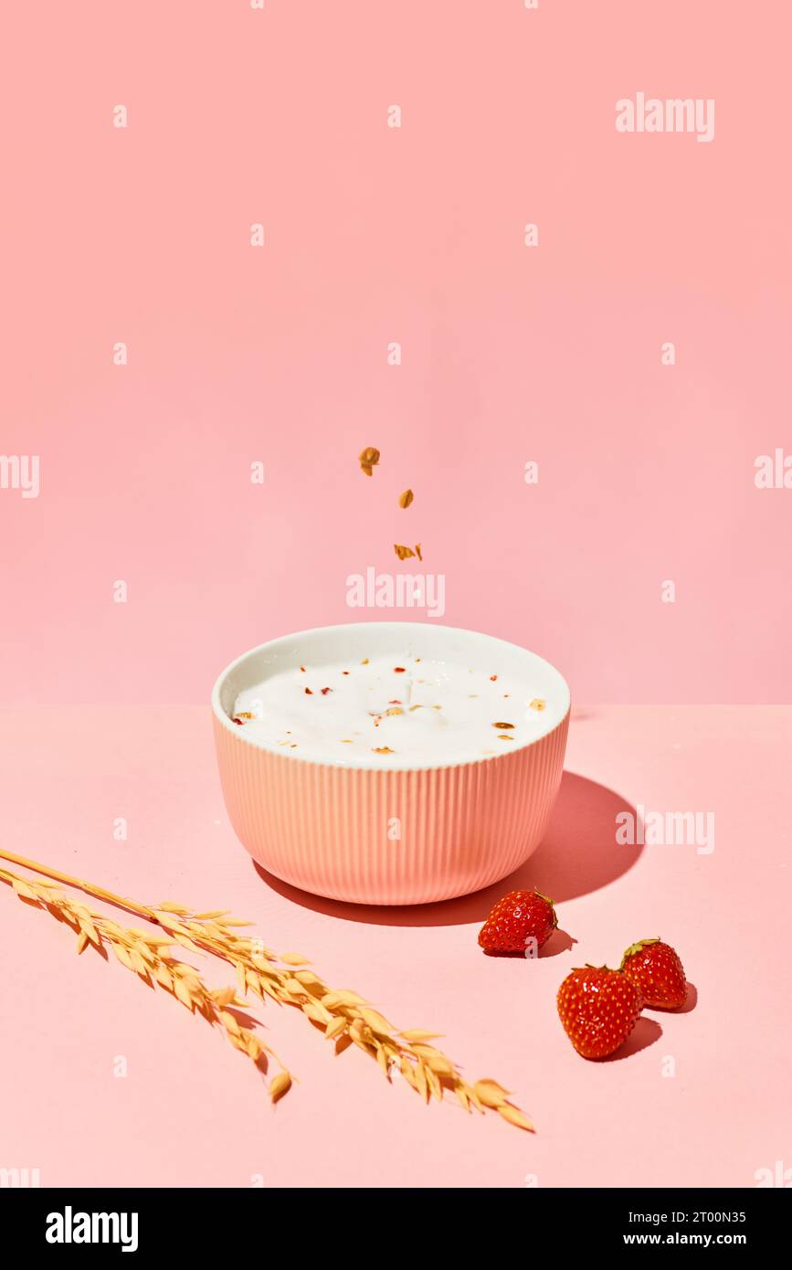 Bowl with muesli, cereal and warm milk against pink background with