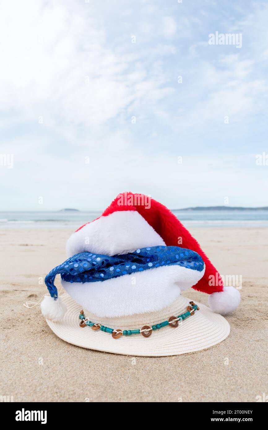 Stack of three hats on the beach. A red Christmas hat, a blue Santa hat ...