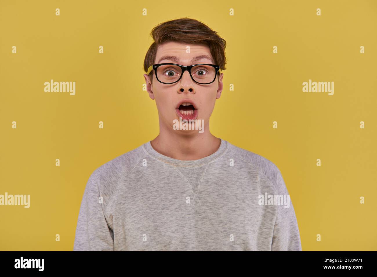 surprised young man in casual comfortable attire and glasses looking at camera with open mouth Stock Photo