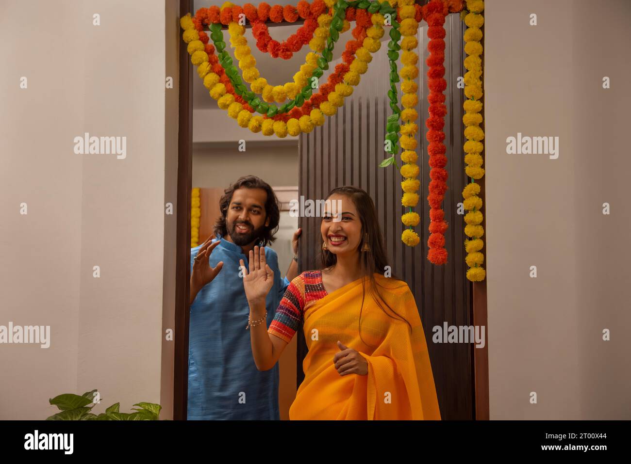 Cheerful excited and surprised couple welcoming and greeting friends  during  Diwali celebrations  at the entrance of their own home Stock Photo