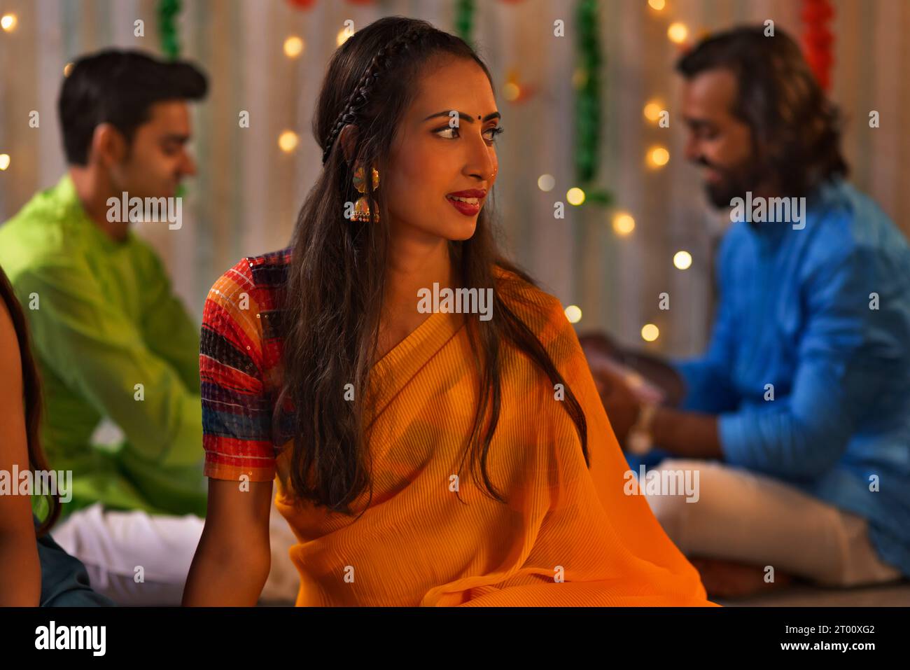 Young woman in yellow saree sitting and looking away and her friends sitting behind Stock Photo