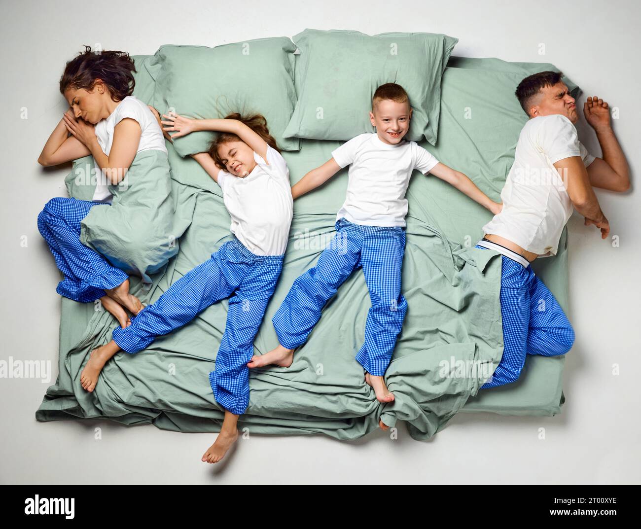 Top view of people covered with blanket lying in bed. Children lying crossed bed and parents on