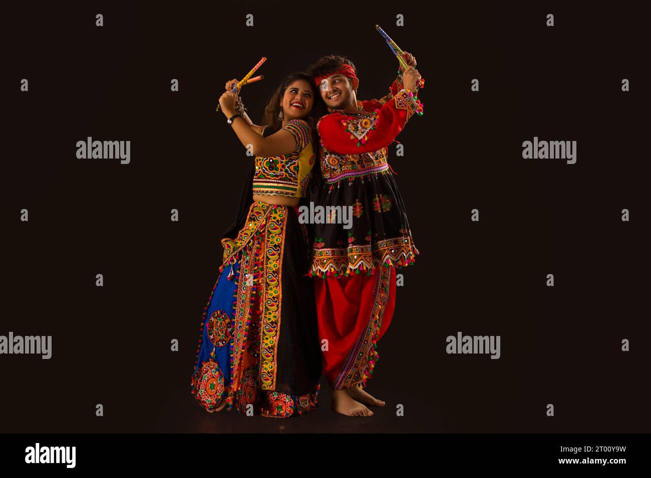 Portrait of happy young couple performing Dandiya Raas on a black ...