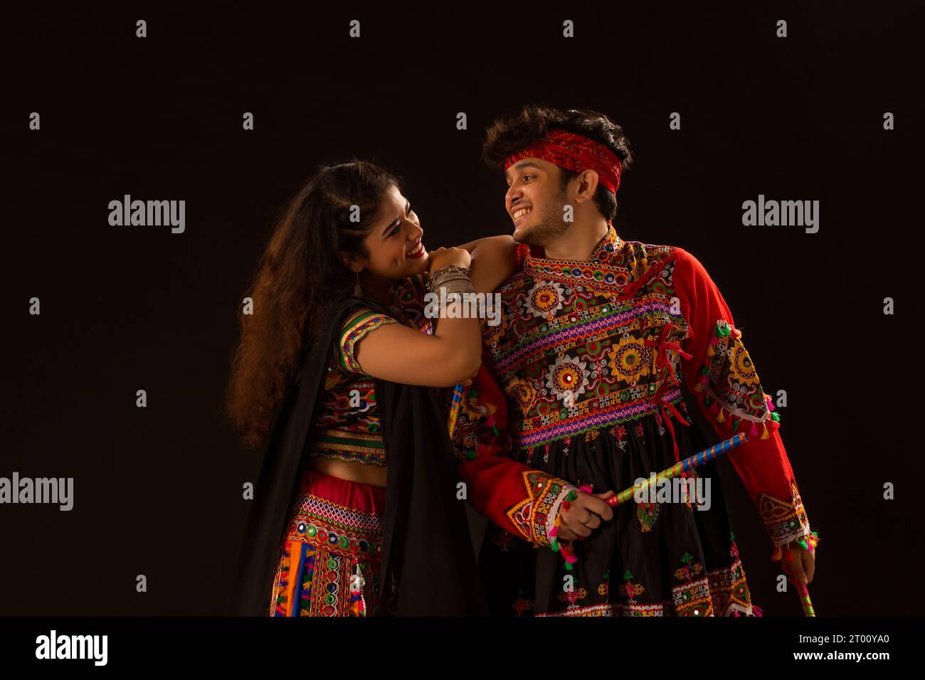 Portrait of happy young couple performing Dandiya Raas on a black ...