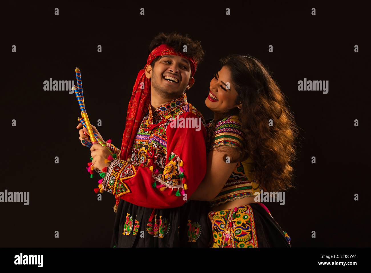 Portrait of happy young couple performing Dandiya Raas on a black ...