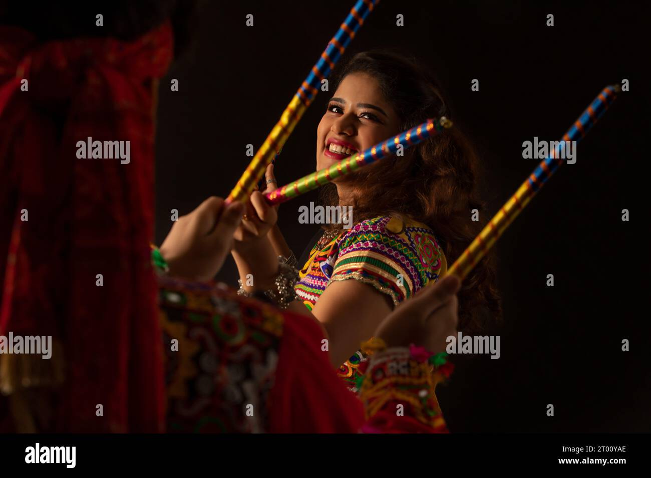 A happy young couple performing Dandiya Raas on a black background ...