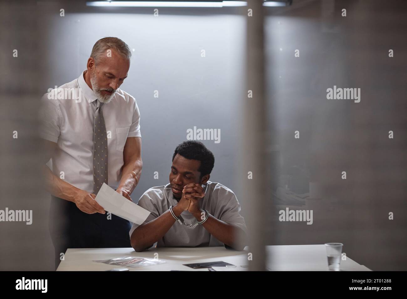 Evidence Box Interrogation Portrait of young Black man in interrogation room with senior detective ...